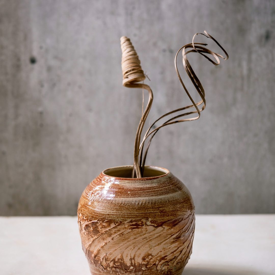 Dry flowers and twigs branch in brown ceramic vase on white marble table with gray wall behind. Copy space.